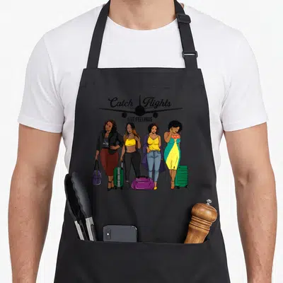 Catch travel aprons - Four women with luggage under Catch Flights text and airplane silhouette in cartoon style — shown on a black cotton canvas apron against a white background
