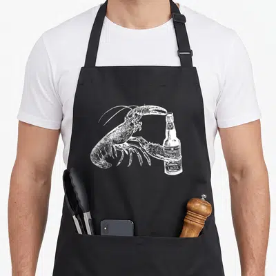 Lobster craft apron - White line art of a lobster standing next to a lager bottle with one claw resting on the cap — shown on a black cotton canvas apron against a white background