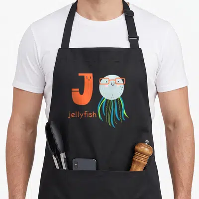 Jellyfish letter animal apron - Large orange letter J next to a grey cartoon jellyfish with glasses and blue green — shown on a black cotton canvas apron against a white background