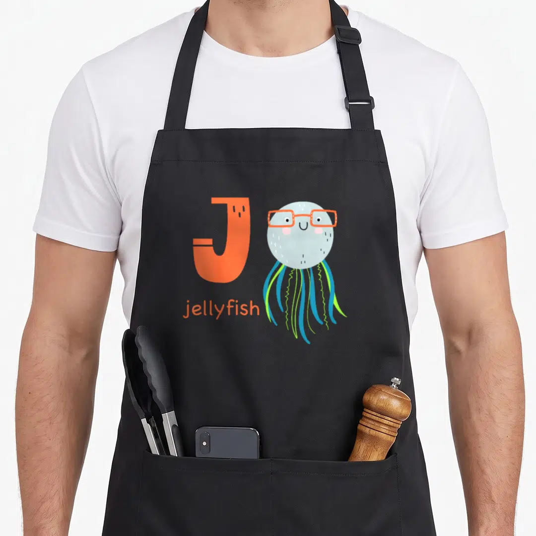 Jellyfish letter animal apron - Large orange letter J next to a grey cartoon jellyfish with glasses and blue green — shown on a black cotton canvas apron against a white background