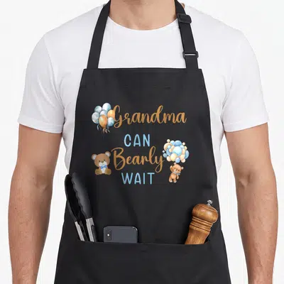 Bearly grandma apron - Teddy bear holding blue balloons with Grandma Can Bearly Wait text — shown on a black cotton canvas apron against a white background