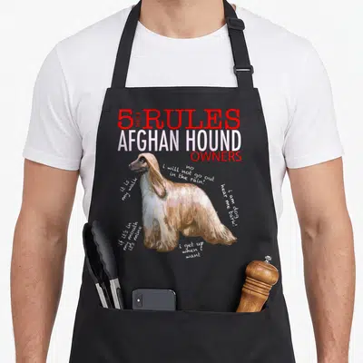 Rule afghan apron - Cartoon Afghan hound surrounded by humorous rule text in red and white — shown on a black cotton canvas apron against a white background