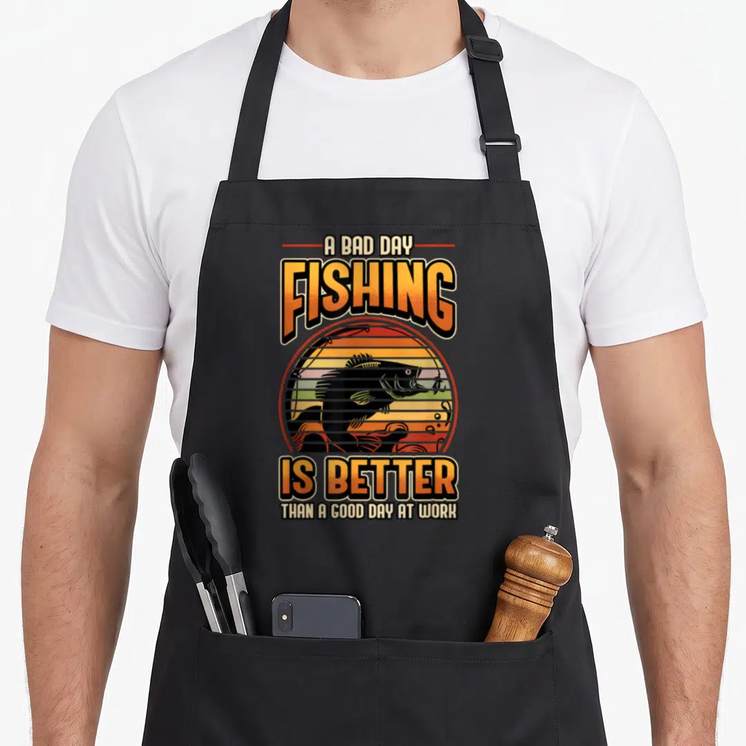 Better fisher fishing aprons - Retro sun graphic with black fish silhouette and orange gradient text reading A BAD DAY — shown on a black cotton canvas apron against a white background
