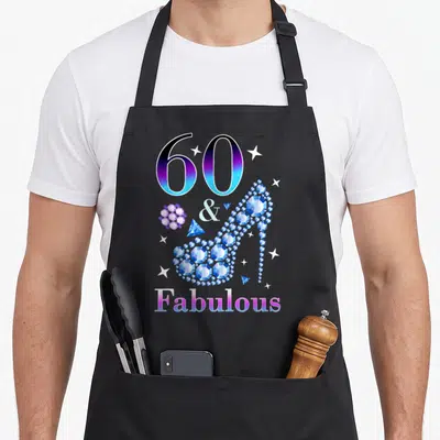 Cute fabulous 60th birthday apron - Gradient 60 & Fabulous text with a diamond high heel shoe and scattered stars — shown on a black cotton canvas apron against a white background