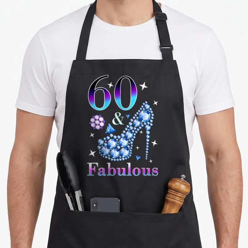 Cute fabulous 60th birthday apron - Gradient 60 & Fabulous text with a diamond high heel shoe and scattered stars — shown on a black cotton canvas apron against a white background