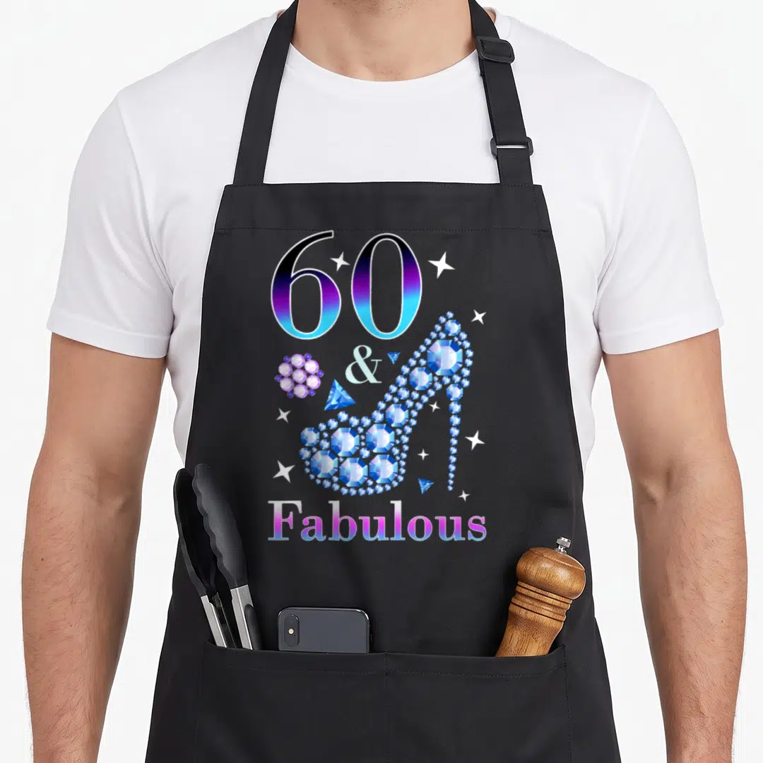Cute fabulous 60th birthday apron - Gradient 60 & Fabulous text with a diamond high heel shoe and scattered stars — shown on a black cotton canvas apron against a white background