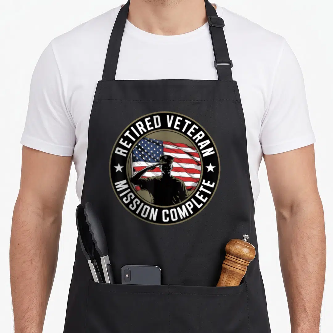 Retired patriotic apron - Circular emblem with saluting soldier, waving flag, and white text on black background — shown on a black cotton canvas apron against a white background