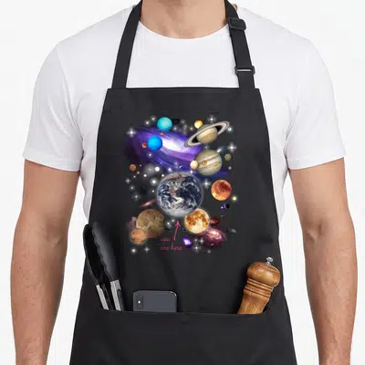 Funny solar space planets apron - Realistic Earth surrounded by planets and purple galaxy with pink you are here text — shown on a black cotton canvas apron against a white background