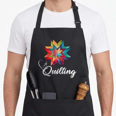 Quiltiing quilter apron - Multicolored quilt star above white Quilting text with heart and flower overlay — shown on a black cotton canvas apron against a white background