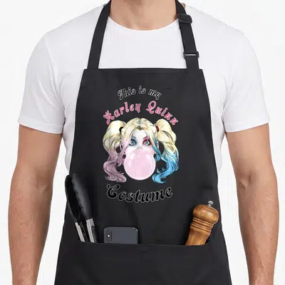 Costume vehicle apron - Harley Quinn face blowing pink bubblegum with split pink and blue hair pigtails — shown on a black cotton canvas apron against a white background