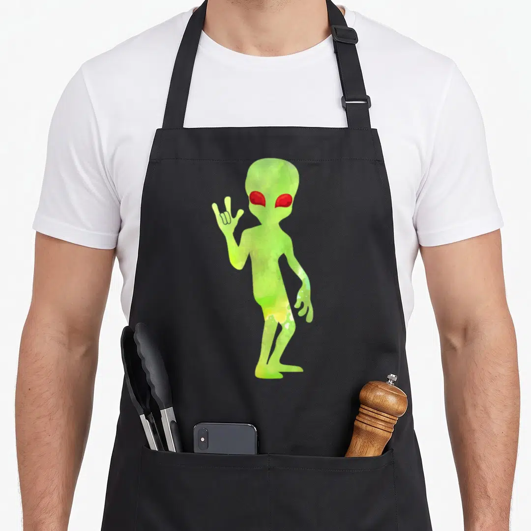 Alien teacher apron - Green watercolor alien with red eyes raising right hand in I Love You sign — shown on a black cotton canvas apron against a white background