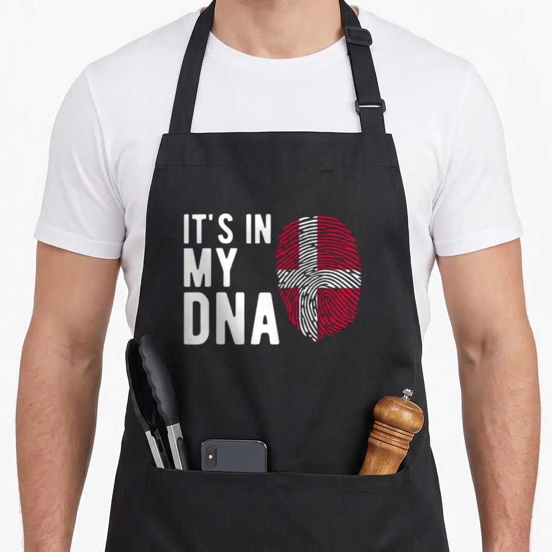 Dna danish apron - IT'S IN MY DNA text next to red and white fingerprint shaped like Danish flag — shown on a black cotton canvas apron against a white background