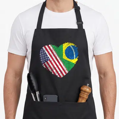 Brazil pride american flag apron - Distressed heart split diagonally showing USA and Brazil flags with Ordem e — shown on a black cotton canvas apron against a white background