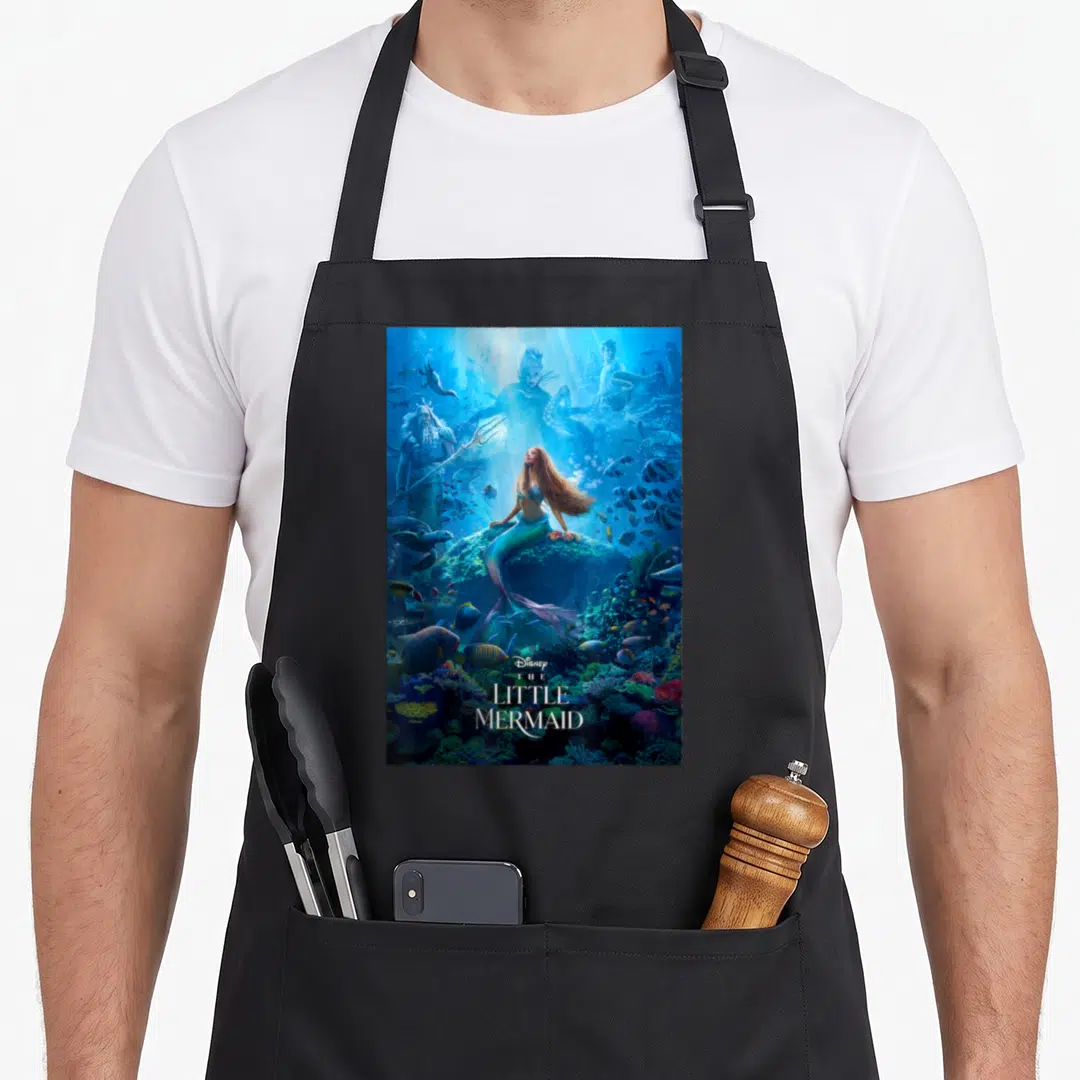 Live mermaid apron - Mermaid on rock with blue teal red photo and stacked Little Mermaid title text — shown on a black cotton canvas apron against a white background