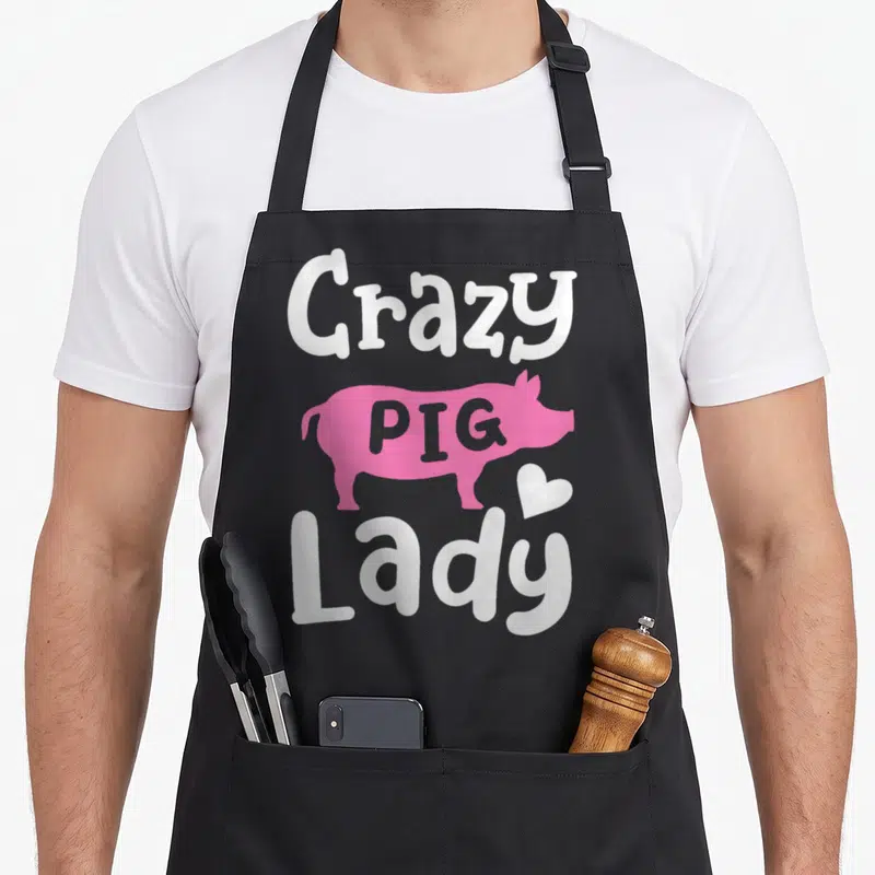 Comfort crazy pig lady apron - Pink pig silhouette with Crazy PIG Lady text and small heart in cartoon style — shown on a black cotton canvas apron against a white background