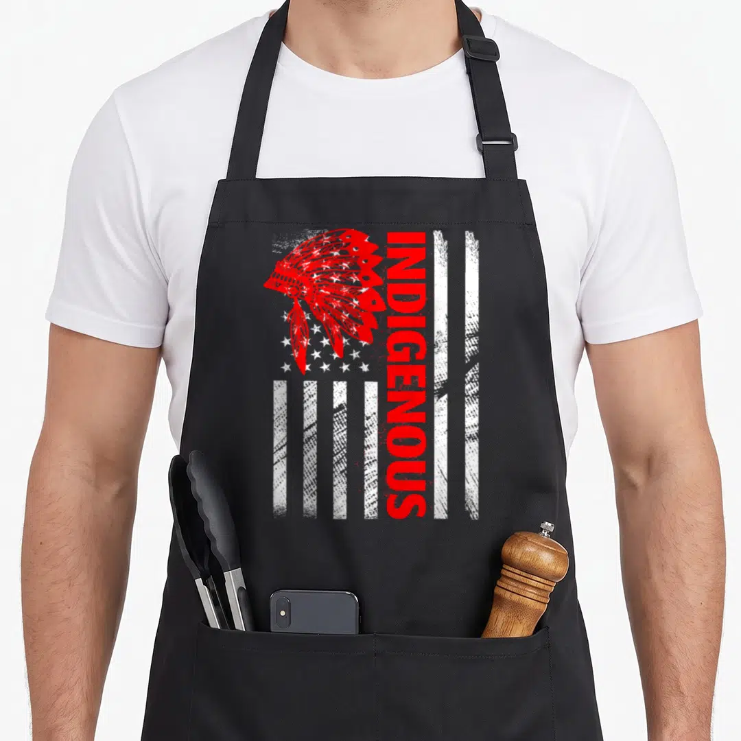 Indigenous distressed apron - Red headdress overlapping white distressed flag with vertical INDIGENOUS text — shown on a black cotton canvas apron against a white background