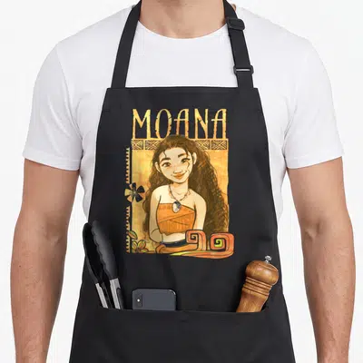 Artistic kitchen island apron - Cartoon Moana portrait with tribal border, orange background, and flower accent — shown on a black cotton canvas apron against a white background