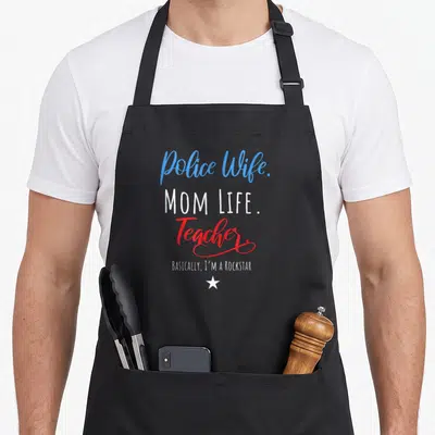 Police best teacher apron - Stacked text Police Wife MOM LIFE Teacher Basically I'm A Rockstar with white star in blue — shown on a black cotton canvas apron against a white background