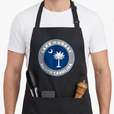 Murray pride apron - Blue circle with white palm tree and moon surrounded by text ring — shown on a black cotton canvas apron against a white background