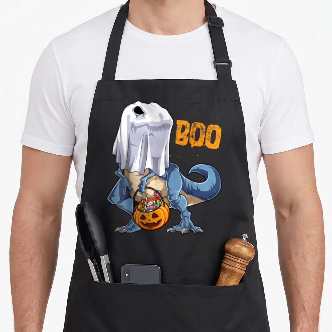 Dinosaur halloween apron - Blue dinosaur in white sheet holding orange pumpkin bucket with BOO text — shown on a black cotton canvas apron against a white background