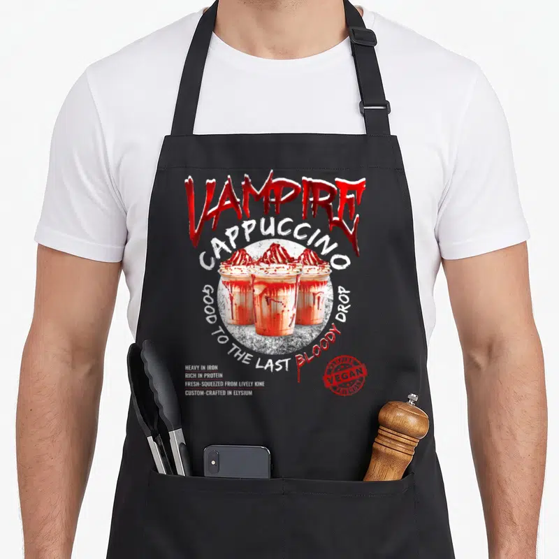 Vampire bloody apron - Three cappuccinos with red syrup and text Vampire Cappuccino Good To The Last Bloody Drop — shown on a black cotton canvas apron against a white background