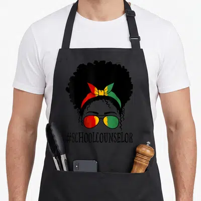 Counselor messy aprons - Stylized woman's head with afro, red yellow green headband and sunglasses above — shown on a black cotton canvas apron against a white background