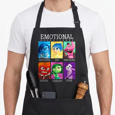 Emotion yearbook apron - Grid of Sadness Joy Bing Bong Anger Disgust Fear portraits with Emotional Adventurers text — shown on a black cotton canvas apron against a white background