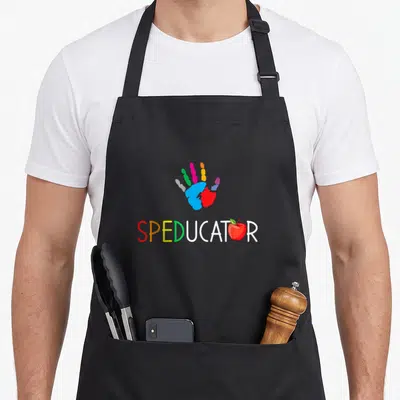 Squad education apron - Multi-colored handprint above SPEDUCATOR text with red apple replacing the O letter — shown on a black cotton canvas apron against a white background