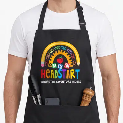 Early preschool teacher apron - Yellow pencil arch with paperclips, apple, ABC blocks, and multi-colored Headstart text — shown on a black cotton canvas apron against a white background