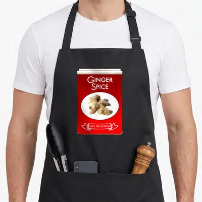 Ginger spice apron - Red spice tin graphic with beige ginger root photo and white ribbon text — shown on a black cotton canvas apron against a white background