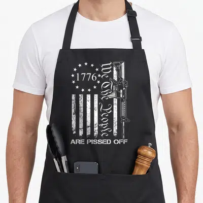 Pissed pro apron - White rifle, stars, stripes, and 1776 We the People Are Pissed Off text on black fabric — shown on a black cotton canvas apron against a white background