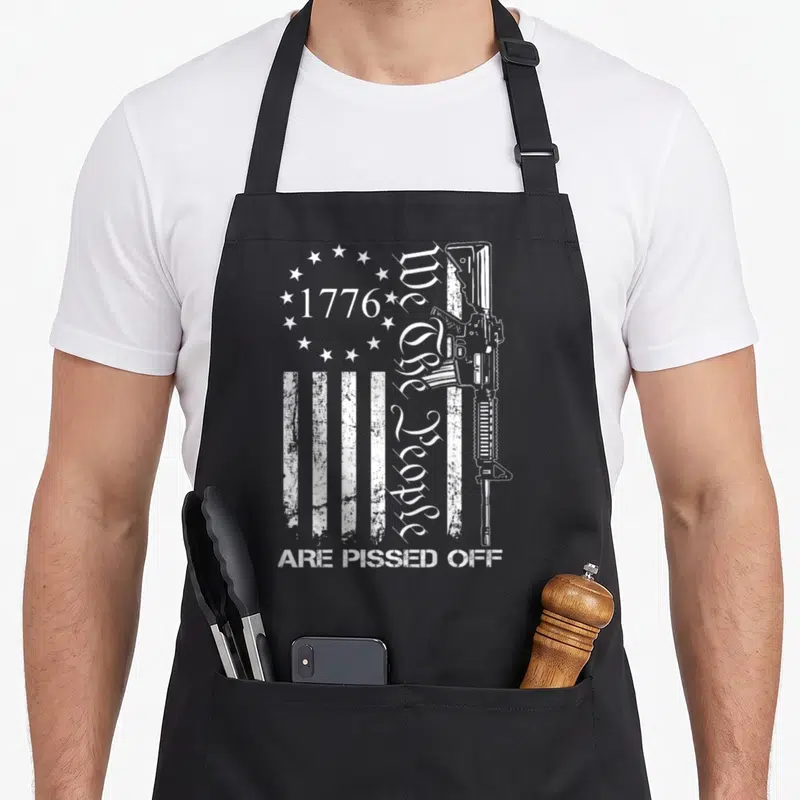 Pissed pro apron - White rifle, stars, stripes, and 1776 We the People Are Pissed Off text on black fabric — shown on a black cotton canvas apron against a white background