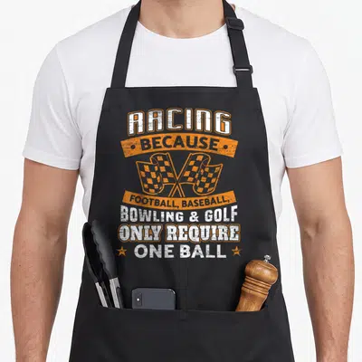 Ball car apron - Racing because one ball text with crossed checkered flags and distressed white orange font — shown on a black cotton canvas apron against a white background