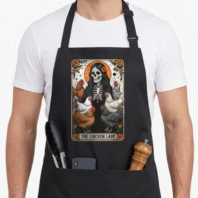 Tarot chicken apron - Skeleton woman with six chickens and THE CHICKEN LADY banner in floral border — shown on a black cotton canvas apron against a white background