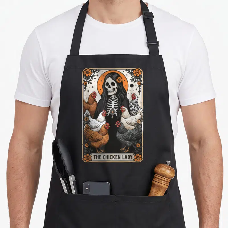 Tarot chicken apron - Skeleton woman with six chickens and THE CHICKEN LADY banner in floral border — shown on a black cotton canvas apron against a white background