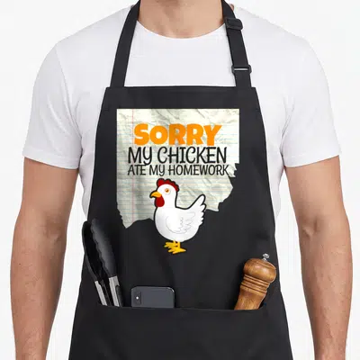 Ate chicken apron - Cartoon white chicken on crumpled lined paper with text SORRY MY CHICKEN ATE MY HOMEWORK — shown on a black cotton canvas apron against a white background