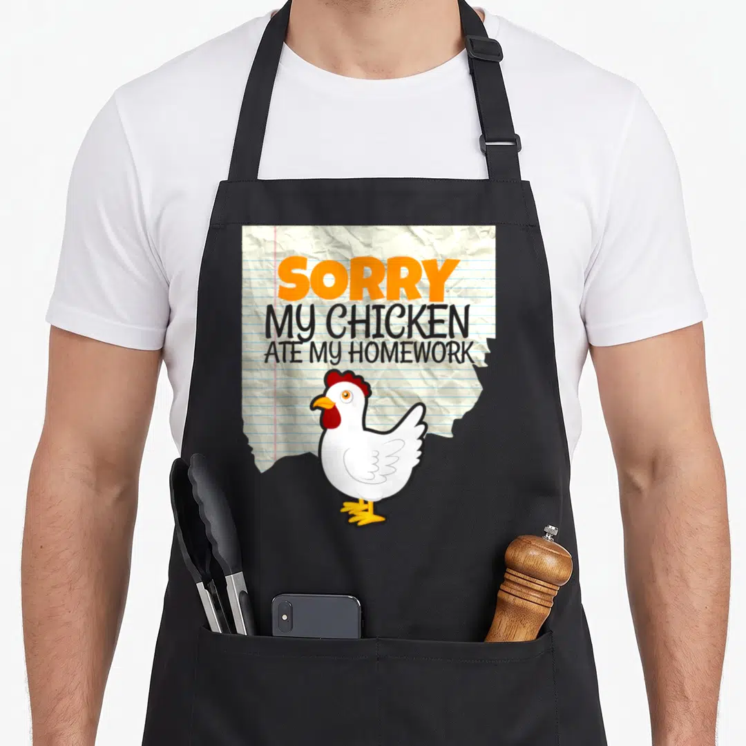 Ate chicken apron - Cartoon white chicken on crumpled lined paper with text SORRY MY CHICKEN ATE MY HOMEWORK — shown on a black cotton canvas apron against a white background