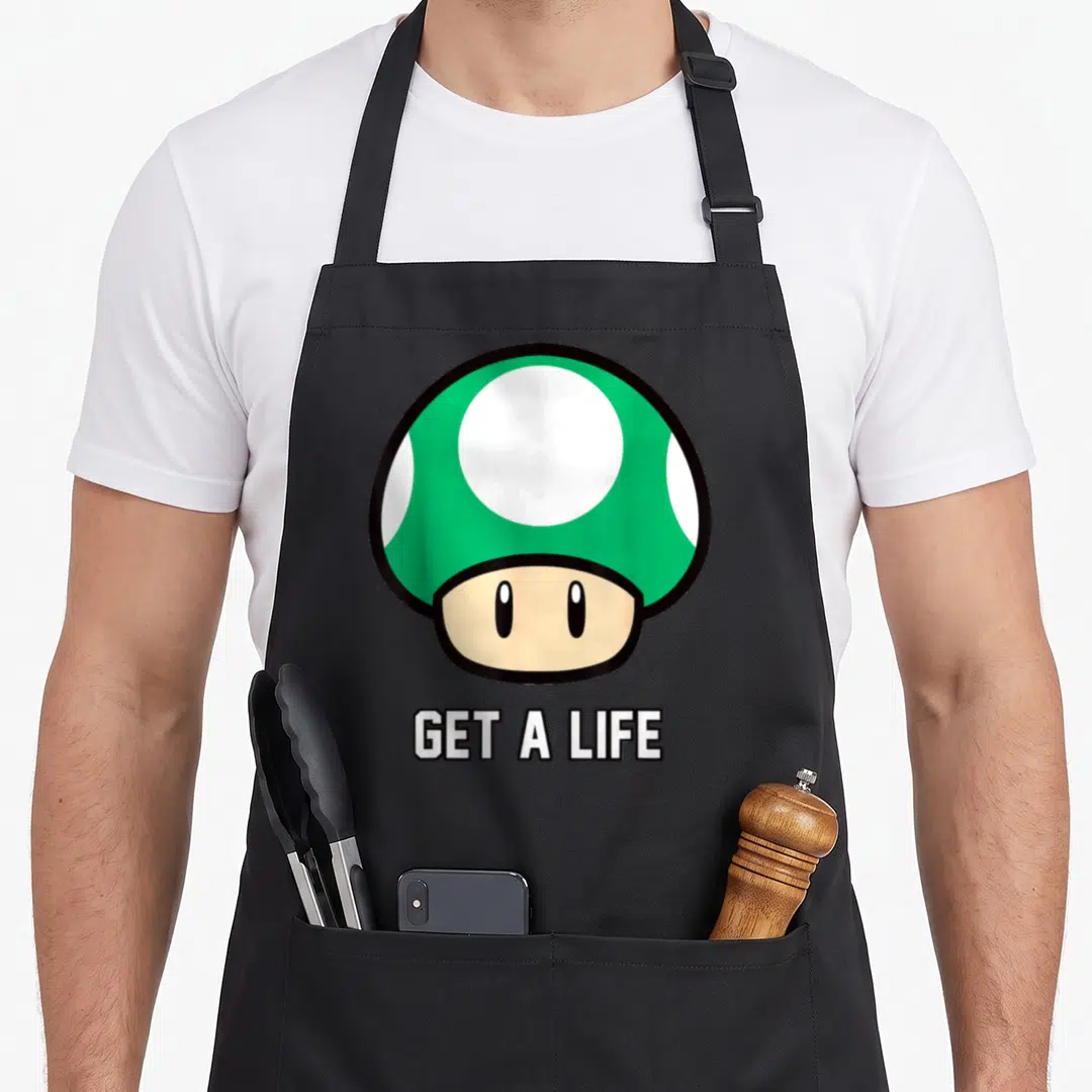 Cute mushroom apron - Green spotted cartoon mushroom above white get a life text — shown on a black cotton canvas apron against a white background