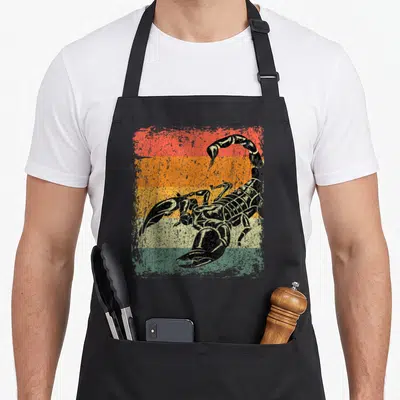 Cute scorpion apron - Black scorpion illustration over five horizontal stripes in red orange yellow and green — shown on a black cotton canvas apron against a white background