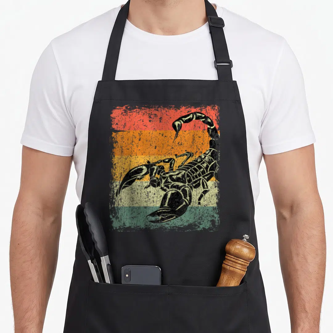 Cute scorpion apron - Black scorpion illustration over five horizontal stripes in red orange yellow and green — shown on a black cotton canvas apron against a white background