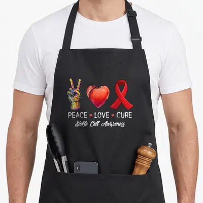 Peace sickle cell awareness apron - Watercolor peace sign heart and red ribbon with PEACE LOVE CURE text — shown on a black cotton canvas apron against a white background