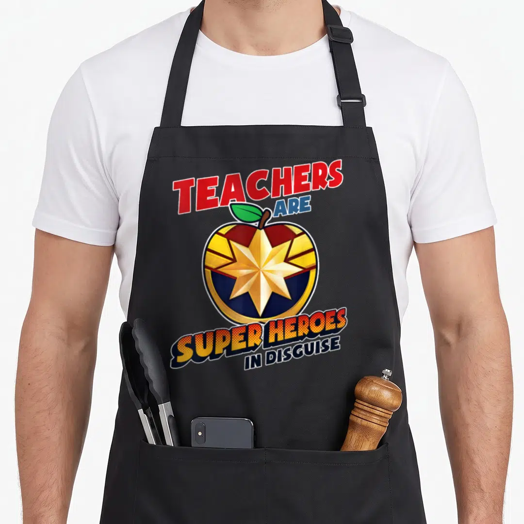 Disguise teacher apron - Cartoon red apple with gold star and TEACHERS ARE SUPER HEROES IN DISGUISE text — shown on a black cotton canvas apron against a white background