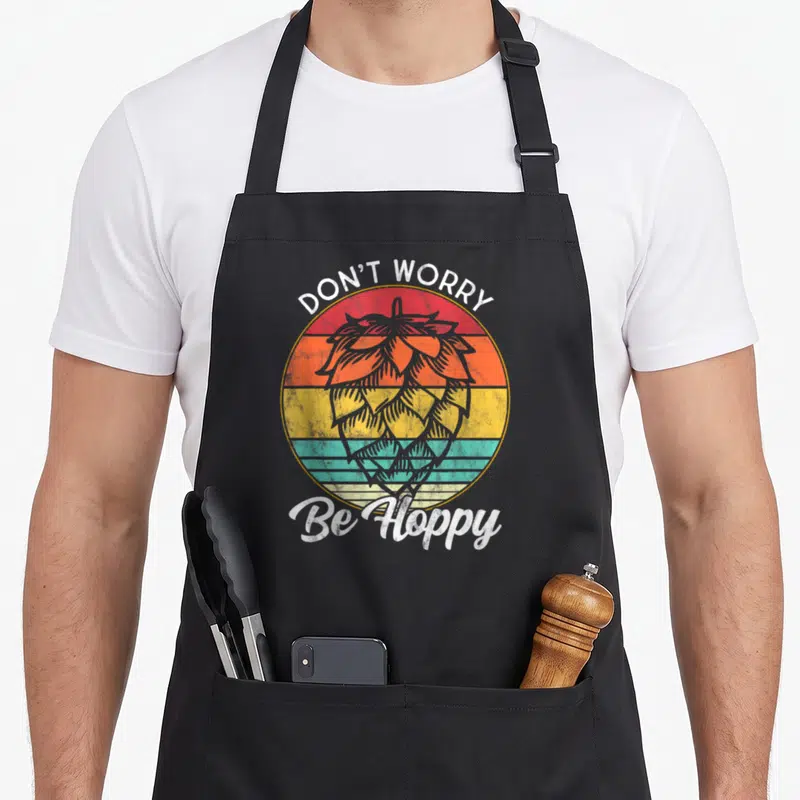 Ipa craft apron - Retro hop cone over red orange yellow teal stripes with Don't Worry Be Hoppy text — shown on a black cotton canvas apron against a white background