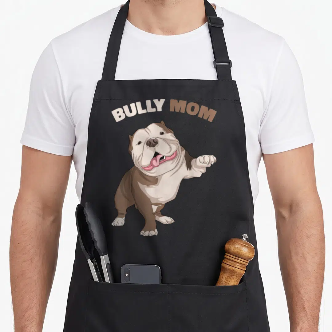 Bully dog mom apron - Cartoon bulldog with arched BULLY MOM text in brown, white, and pink — shown on a black cotton canvas apron against a white background
