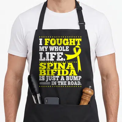 Myelomeningocele spina bifida awareness apron - Yellow ribbon and white text I fought my whole life spina bifida is — shown on a black cotton canvas apron against a white background