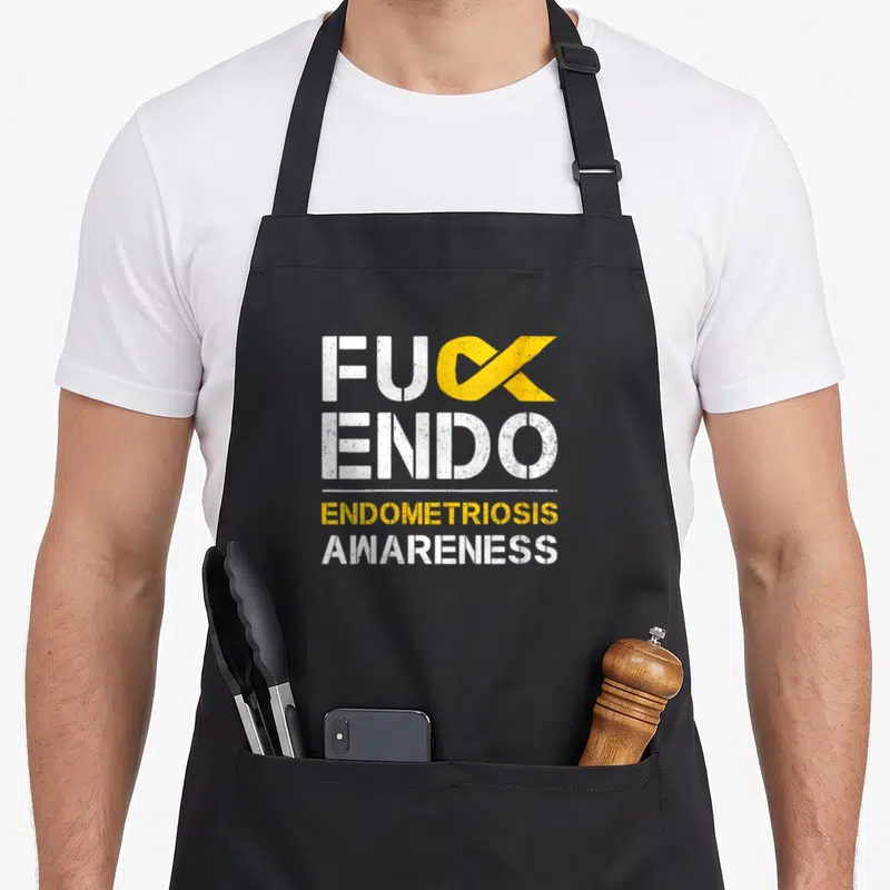 Endometriosis awareness ribbon apron - FUCK ENDO text with yellow ribbon replacing K and Endometriosis Awareness below — shown on a black cotton canvas apron against a white background