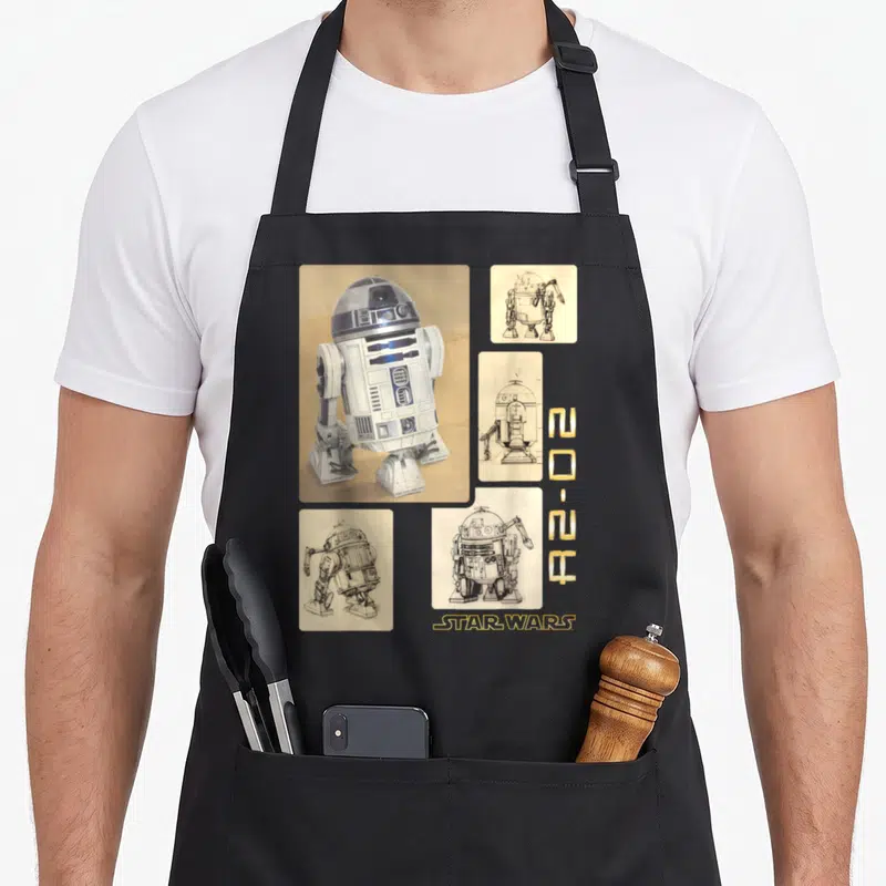 Sketch boxed apron - R2-D2 photo with four technical sketches and gold vertical symbols — shown on a black cotton canvas apron against a white background