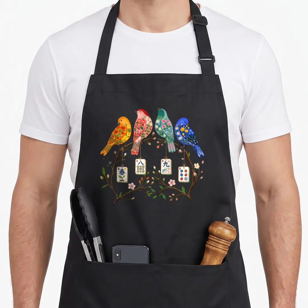 Mahjong the floral apron - Four birds on branch with mahjong tiles showing Spring, 8, 9, 6 characters and flowers — shown on a black cotton canvas apron against a white background