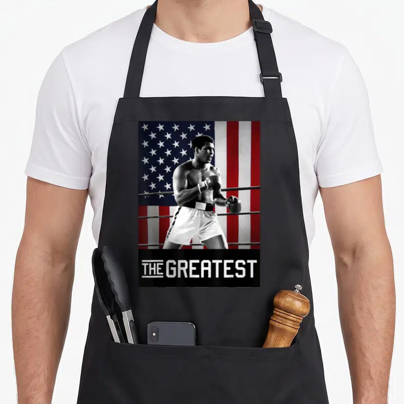 Muhammad mahamri apron - Boxer photo with THE GREATEST text on black bar against flag background — shown on a black cotton canvas apron against a white background