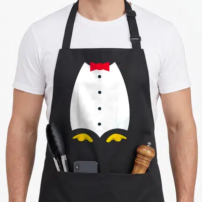 Tuxedo penguin aprons - Cartoon tuxedo with red bow tie, four black buttons, and two yellow feet — shown on a black cotton canvas apron against a white background